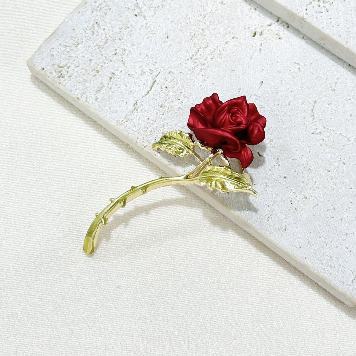 Red rose brooch displayed on table image 7